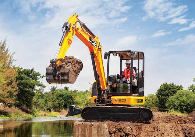 JCB 55z mini excavator in action moving dirt with a full shovel load.